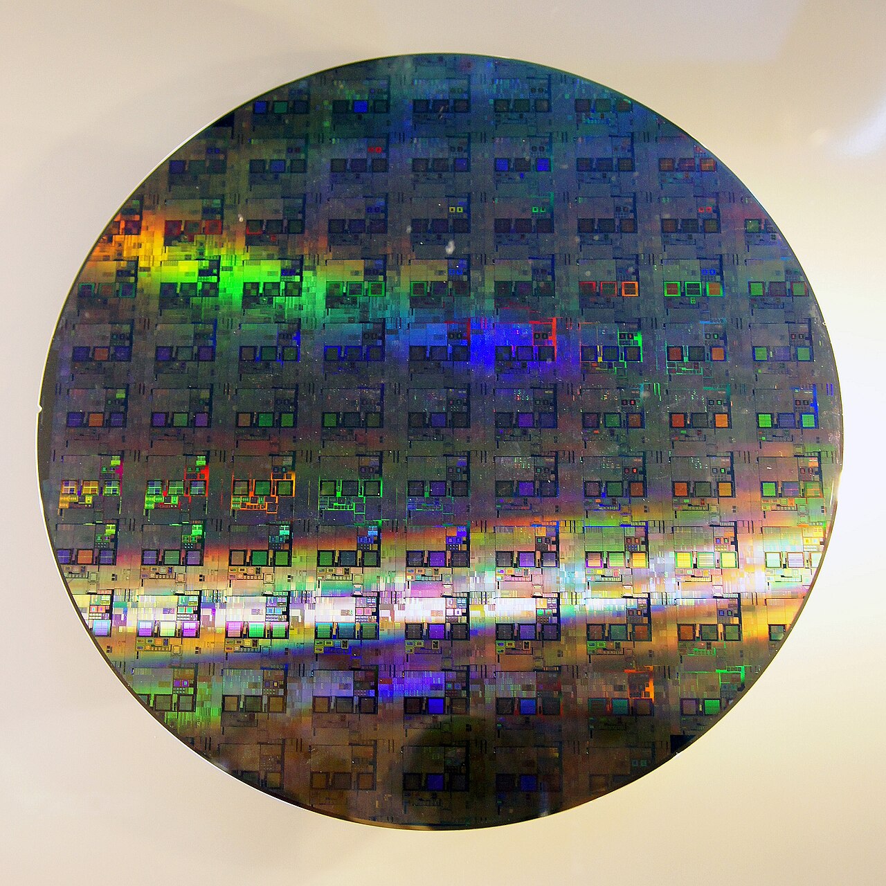 Close-up of a 12-inch silicon wafer etched with chip dies, showing the rainbow interference pattern from lithography