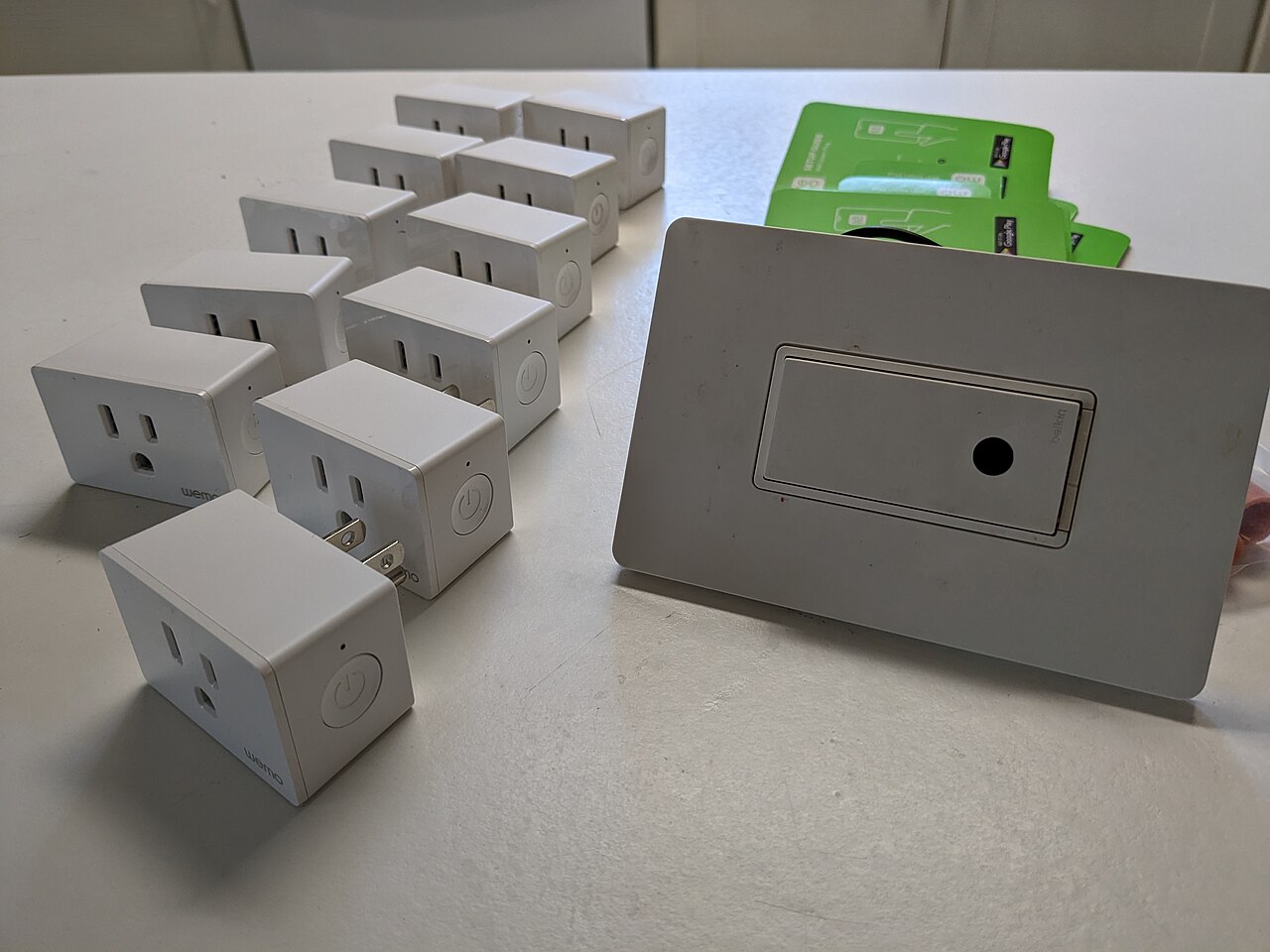 Several Wemo smart plugs of different sizes lined up next to a smart light switch, showing the range of smart plug form factors available