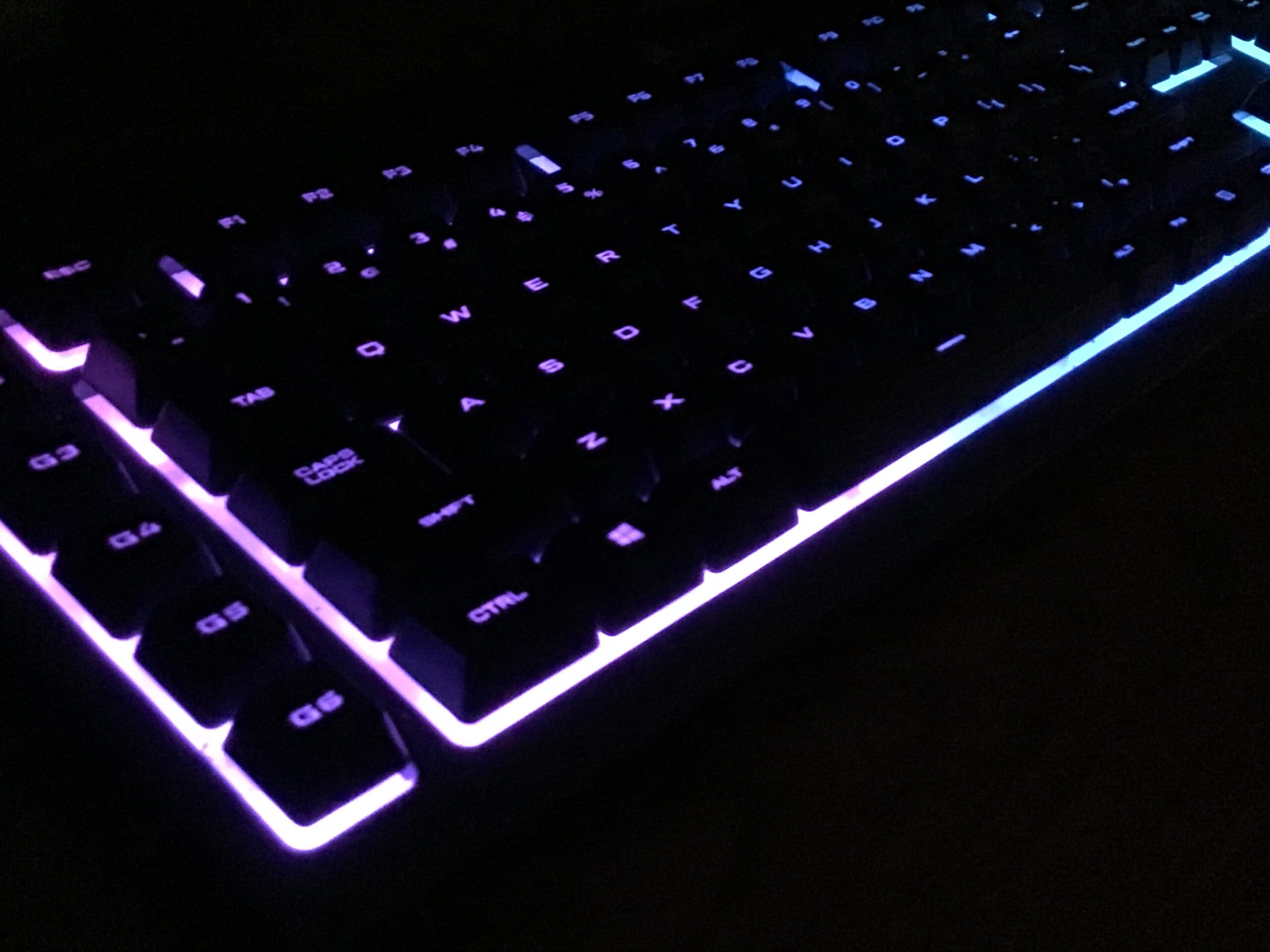 Close-up of a mechanical keyboard with RGB purple and blue backlighting illuminating the keys in a dark environment