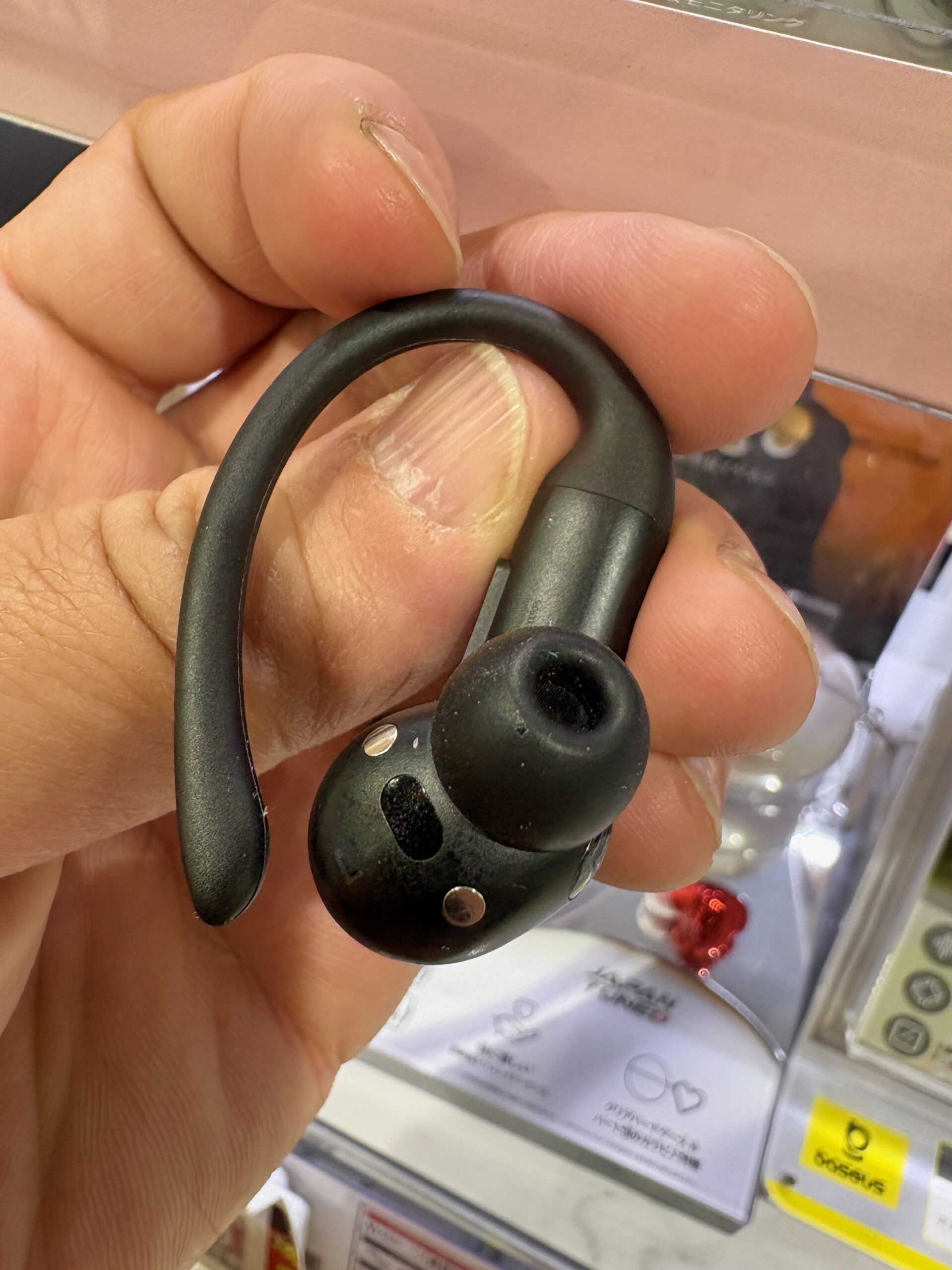Close-up of single wireless earbud with ear hook held in hand at electronics store