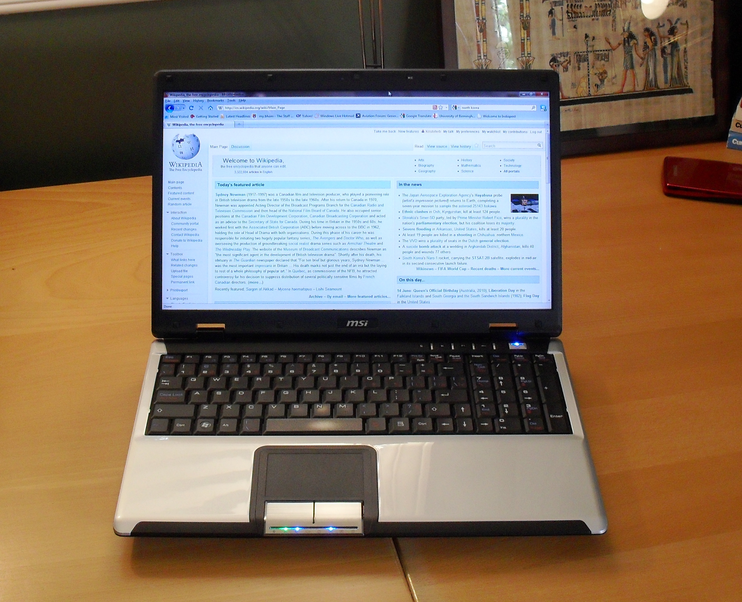 MSI laptop computer open on wooden desk showing Wikipedia website on screen