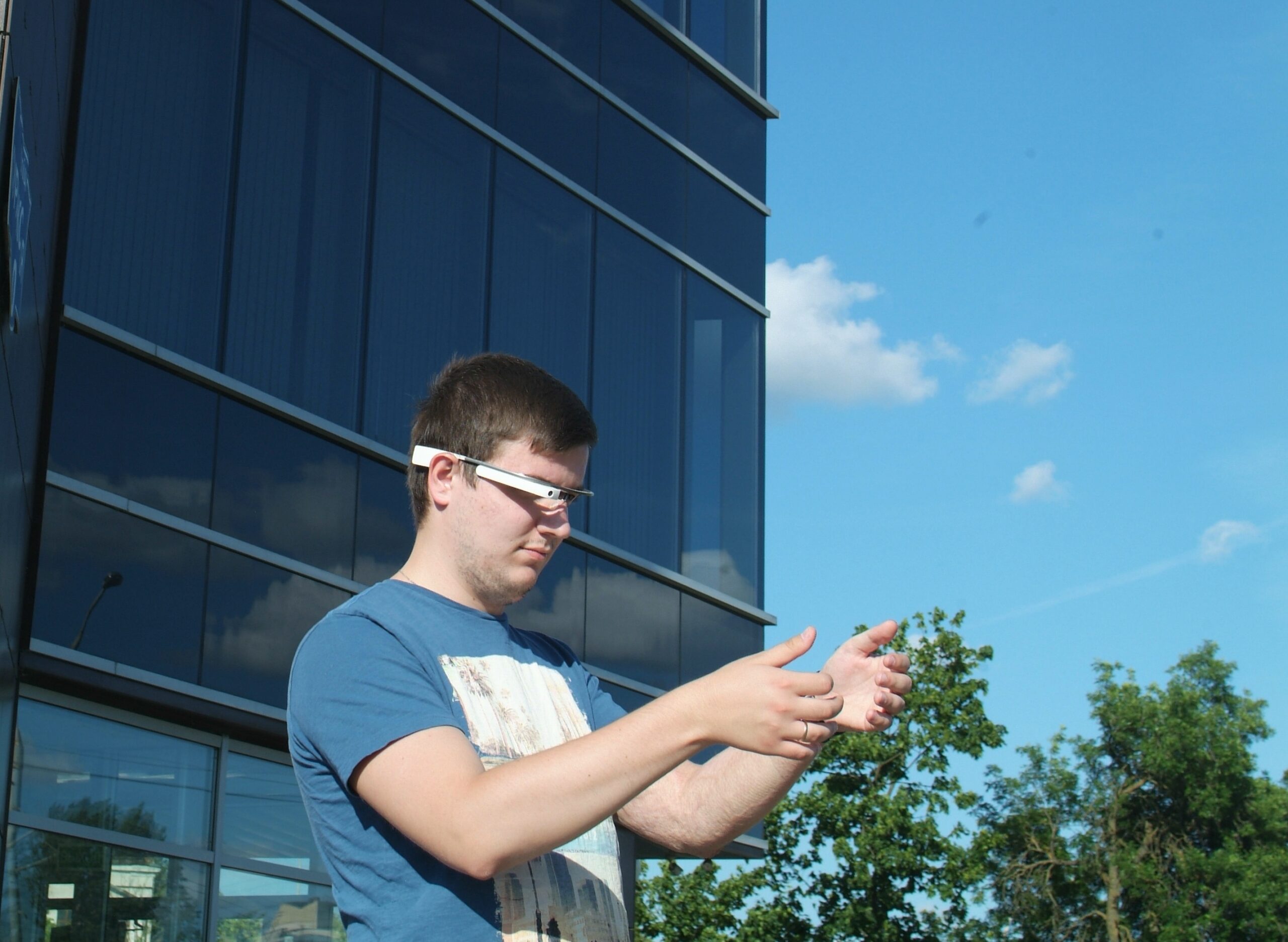 Man wearing Google Glass-style AR glasses outdoors interacting with augmented reality interface
