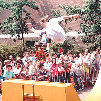 Tony Hawk performing an ollie skateboard trick at a live event in front of a crowd