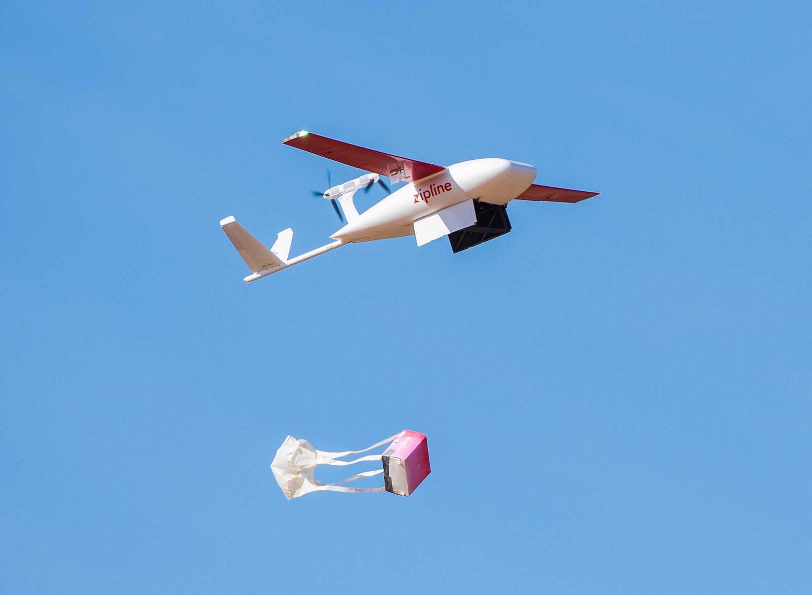 A delivery drone drops a package by parachute, illustrating how drone delivery works