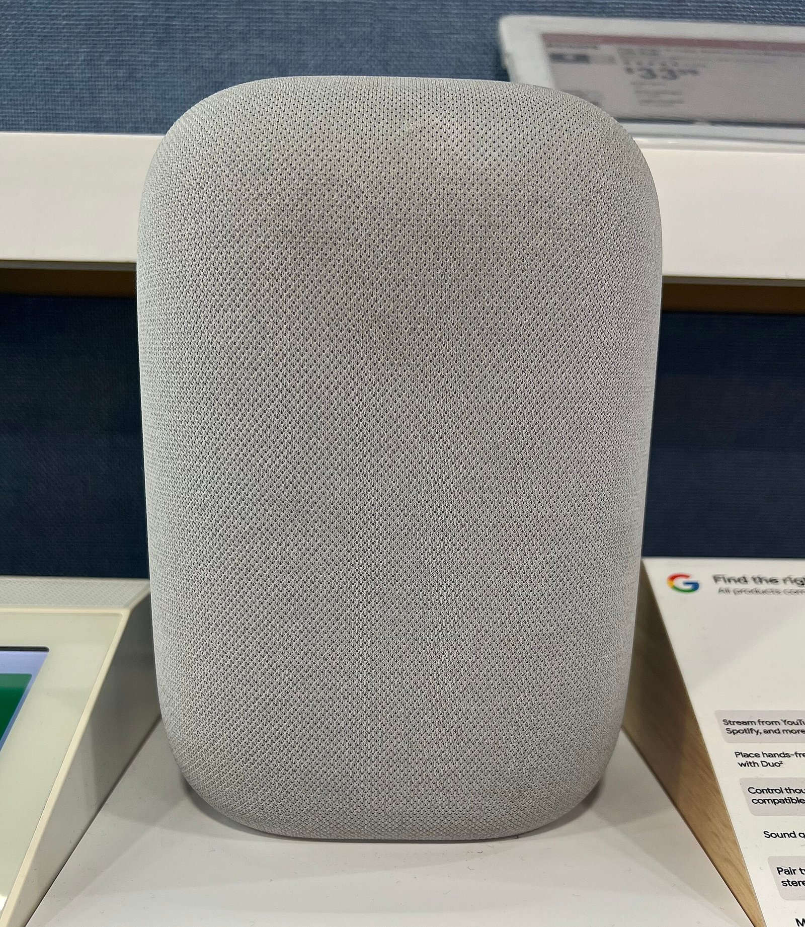 The older Google Nest Audio speaker (2020) in gray fabric finish on display at a Google retail store, the model being replaced by the new 2026 Google Home Speaker