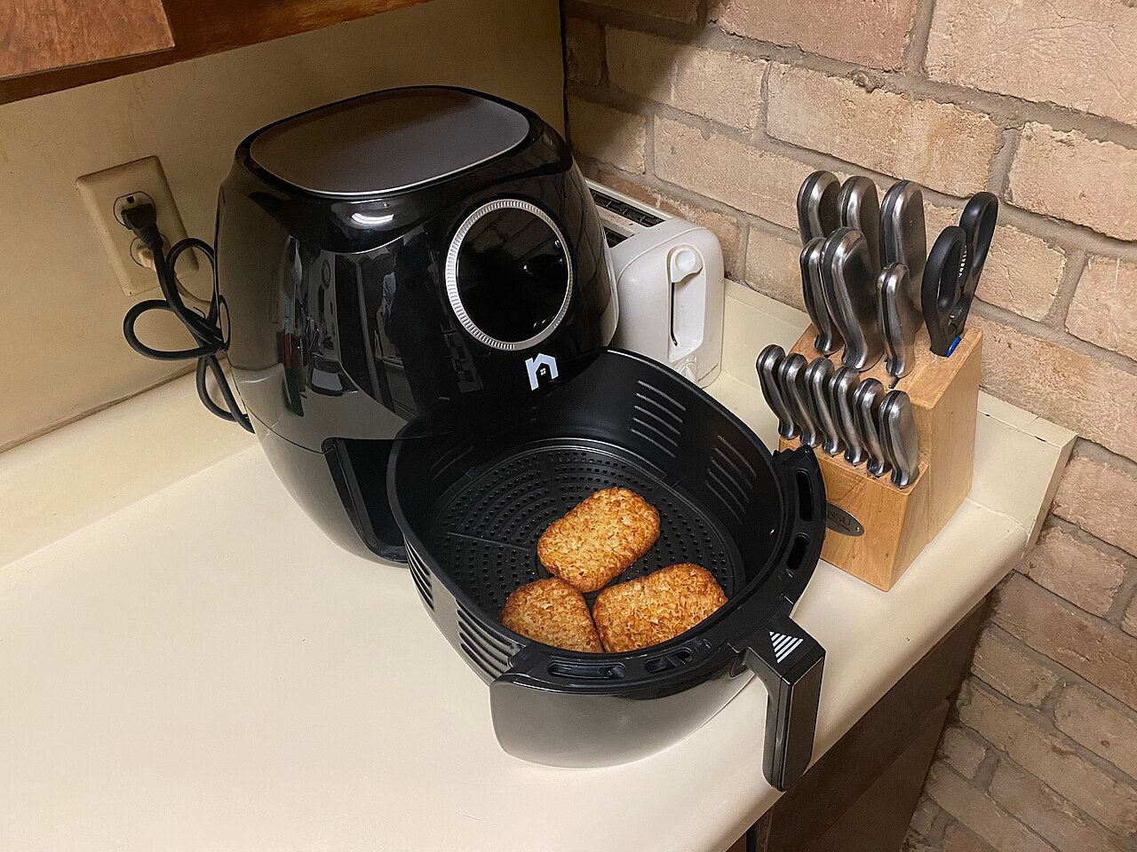 Air fryer basket pulled out on a kitchen counter with hash browns cooking inside, showing food-in-basket use for a family-size batch